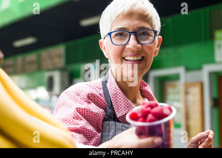 Portrait der älteren Frau verkauft Himbeeren auf dem Markt Stockfoto