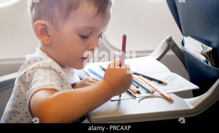 Closeup Portrait von Toddler boy Zeichnung mit bunten pancils am aufklappbaren Tisch im Flugzeug während der langen Flug Stockfoto