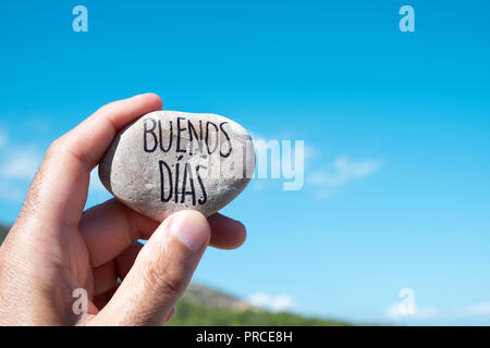Nahaufnahme eines jungen kaukasischen Mann mit einem Stein mit dem Text Buenos dias, guten Morgen auf Spanisch geschrieben, indem sie gegen den blauen Himmel Stockfoto