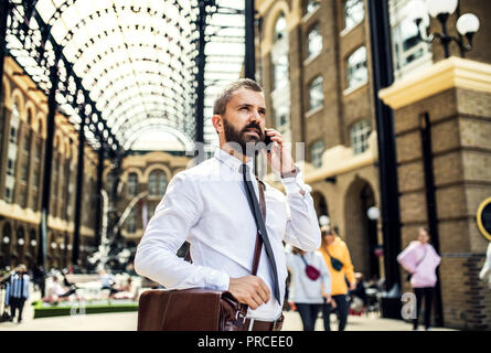 Geschäftsmann mit Smartphone auf dem trian Bahnhof in London, ein Telefonanruf. Stockfoto