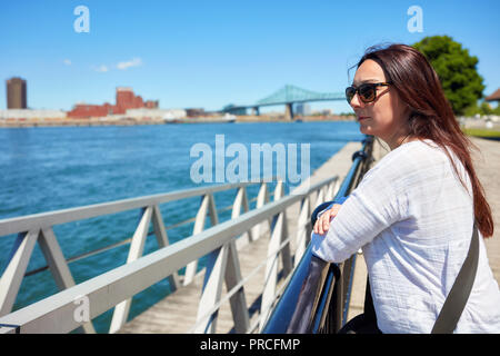 Attraktive rothaarige Frau mit Sonnenbrille auf die Landschaft von Montreal Stadt und der Saint Lawrence River an einem sonnigen Sommertag in Québec, Kanada Stockfoto