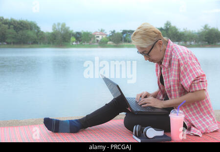 Eine Frau mit Laptop Computer, während am Ufer des Flusses sitzen. Stockfoto