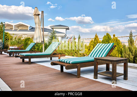 Holz- liege Liegestühle in der Nähe von einem Outdoor Pool unter diffusem Tageslicht am Nachmittag Stockfoto