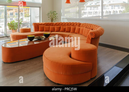 Orange gekrümmte Sofa und Tisch in einem großen, modernen, zeitgenössischen Zimmer. Stockfoto