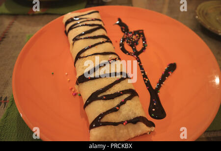 Close-up Choco Banana Filling Crepe dekoriert mit Schokoladensauce serviert auf lebhaften Orange Farbe Platte Stockfoto