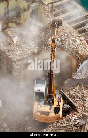 Gebäudeabbruch mit einem Bagger in der Staubwolke, Ansicht von oben. Stockfoto