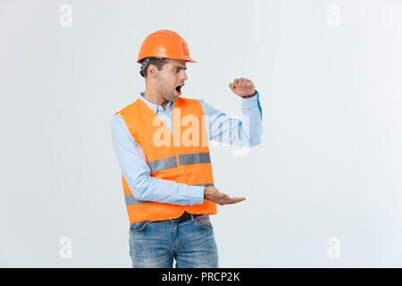 Happy Bart Ingenieur die Hand auf die Seite legen und etwas erklären, Guy tragen caro Shirt und Jeans mit gelber Weste und Helm, orange auf weißem Hintergrund Stockfoto