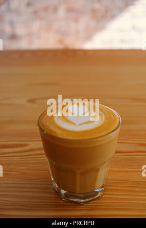 Flache weiße Kaffee. Flache weiße Kaffee in transparenten Glas auf hölzernen Tisch in einem Cafe. Es ist Espresso-Kaffee trinken, bestehend aus Espresso mit schaumstofftasche (gedämpfte Milch mit kleinen, feinen Blasen mit einer glänzenden oder samtige Konsistenz) Stockfoto