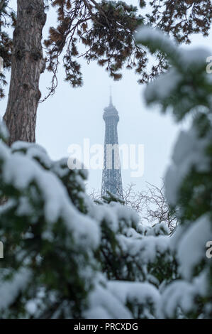 Eiffel Tower unter dem Schnee hinter Bäumen aus den Trocadero Gärten im Winter in Paris, Frankreich Stockfoto