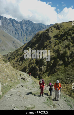 Touristen Trekking in der Nähe der Kirche der Heiligen Dreifaltigkeit Gergeti durch den Fluss Chkheri, unter dem Berg Kazbegi liegt auf einer Höhe von 2170 Metern in den Kaukasus, Georg Stockfoto