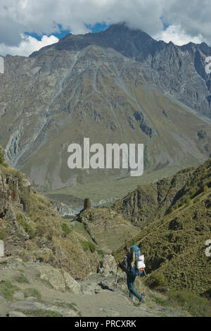 Touristen Trekking in der Nähe der Kirche der Heiligen Dreifaltigkeit Gergeti durch den Fluss Chkheri, unter dem Berg Kazbegi liegt auf einer Höhe von 2170 Metern in den Kaukasus, Georg Stockfoto