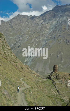 Touristen trekking durch einen Turm in der Nähe der Kirche der Heiligen Dreifaltigkeit Gergeti durch den Fluss Chkheri, unter dem Berg Kazbegi liegt auf einer Höhe von 2170 Metern in den Cauc Stockfoto