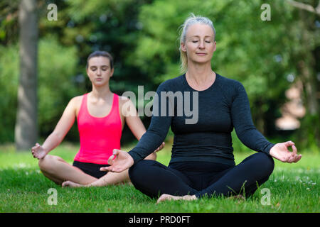 Reifen passen gesunde Frauen mittleren Alters Yogalehrer Yogi außerhalb der Lehre junge Frau bei Yoga Praxis in einer natürlichen ruhigen grünen Umgebung Stockfoto