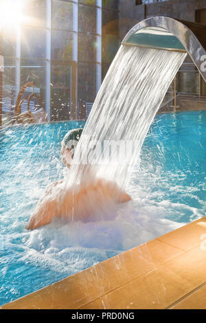 Schöner Mann entspannen im Pool mit Hydromassage Hydrotherapie in einem luxuriösen Hotel mit großen Glasfenstern mit Blick in die Natur. Stockfoto