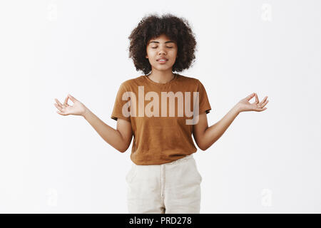 Innen- schuss der Ruhe und des stilvollen pacient urban Studentin mit Afro Frisur und dunkle Haut schließen Augen lächeln sorglose Verbreitung Hände beiseite in zen Geste meditieren und Linderung von Stress Stockfoto