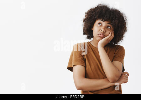 Träumen, wohlhabend und sorgloses Leben. Portrait von Thoughful Spaced Out süße dunkelhäutige Mädchen mit Afro Frisur in Braun t-shirt schiefen Gesicht auf Palm und und schaut, während sie Phantasie Stockfoto