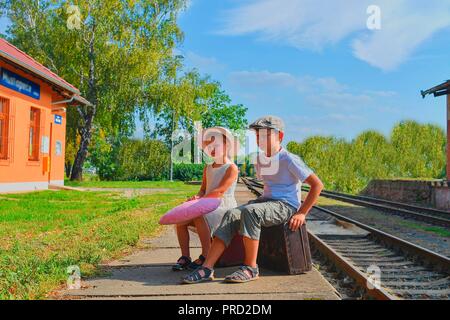 Kleine Kinder - Mädchen und Jungen auf einem Bahnhof und warten auf den Zug mit Vintage Koffer. Reisen, Urlaub und chilhood Konzept. Reisen ins Stockfoto