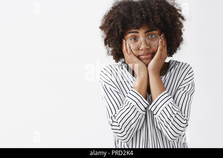 Taille-up Shot der müde und gleichgültig düster düster-Skinng junges Mädchen mit Afro Frisur quetschen Gesicht mit Palmen auf Wangen starrte unvorsichtig und erschöpft von der Kamera träumen über Tag. Stockfoto