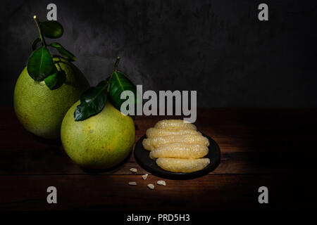 Zwei pomelo und einen Teller mit pomelo Fleisch auf dem Holztisch mit Licht malen Effekt Stockfoto