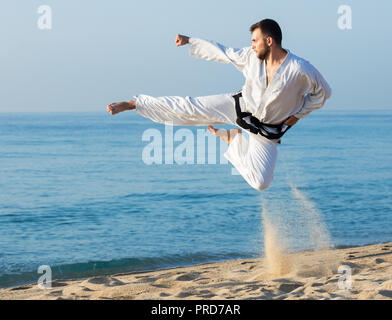 Junger Mann üben Karate stellt am Meer in sonniger Morgen im Freien Stockfoto