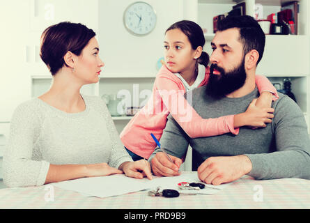 Ernsthafte junge Vater und Mutter Unterzeichnung Scheidung, während ihre Tochter zu Hause Stockfoto