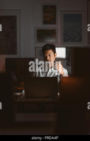 Asiatische Geschäftsmann Kaffee trinken während der Arbeit in einem dunklen Büro Stockfoto