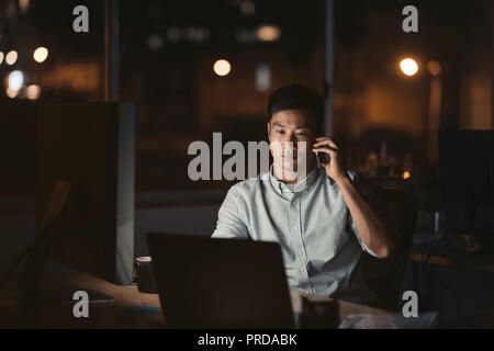 Asiatische Geschäftsmann sprechen über ein Handy in einem dunklen Büro Stockfoto