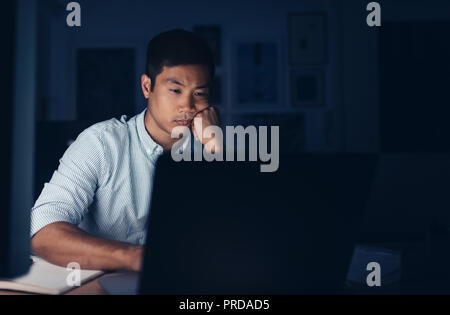 Müde asiatische Geschäftsmann auf einem Laptop spät in der Nacht Stockfoto