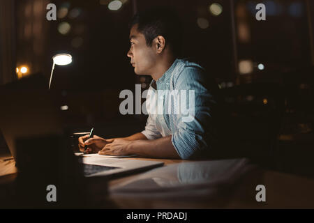 Junge asiatische Geschäftsmann online arbeiten in einem dunklen Büro Stockfoto