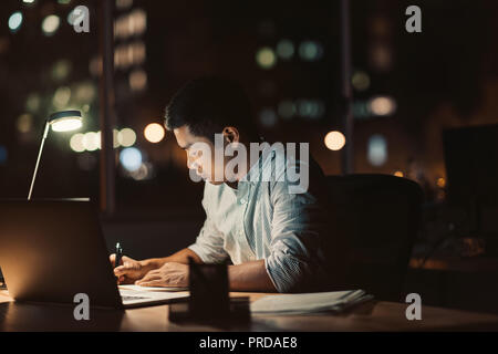 Asiatische Geschäftsmann an seinem Schreibtisch bis spät in den Abend arbeiten Stockfoto