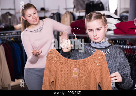 Jugendliche Mädchen eng am neuen Strickpullover suchen während des Einkaufs mit ihrer Mutter in der kleidung shop Stockfoto