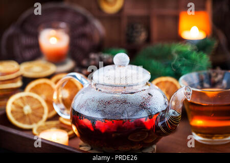 Teekanne aus Glas heißer schwarzer Tee auf gemütlichen Hintergrund mit getrockneten Orangen und Kerzen Stockfoto