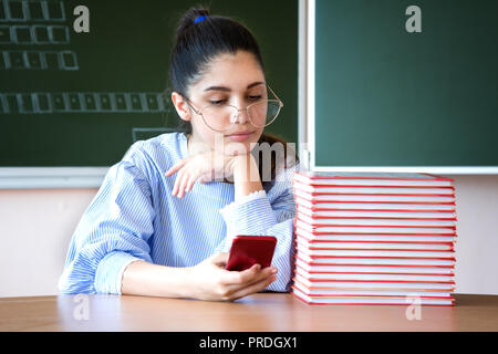Student sitzt gegen Blackboard und schaut auf Mobile Stockfoto