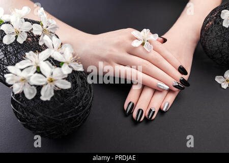 Schwarz und Silber Maniküre mit Cherry Blossom auf schwarzem Hintergrund. Frau mit schwarzen Nägel mit weißen Blumen umgeben. Körperpflege. Hautpflege Stockfoto