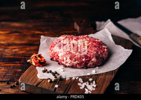 Rohes Rindfleisch Patty mit Gewürzen auf Schneidebrett für Burger. Stockfoto