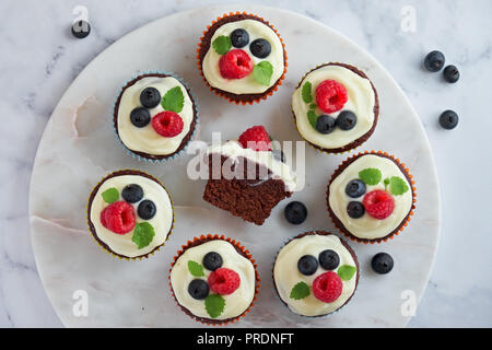 Chocolate Muffins oder kleine Kuchen mit Schlagsahne und Beeren, flach auf weißem Marmor Stein legen Stockfoto