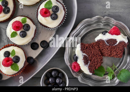 Chocolate Muffins oder kleine Kuchen mit Schlagsahne und Beeren in Metall Teller, flach auf dunklem Holz legen Stockfoto