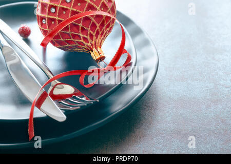 Weihnachtsmenü Konzept mit schwarzem Teller und Besteck mit roten Weihnachten Schmuckstück und Farbband eingerichtet, text Raum Stockfoto