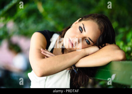 Schöne junge Frau mit blauen Augen in die Kamera sitzt auf städtischen Bank suchen. Girl ith süßen Blick auf Park. Stockfoto