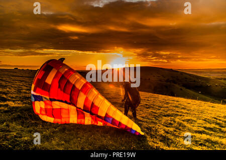 Firle Beacon, Lewes, East Sussex, Großbritannien. Oktober 2018..Gleitschirmflieger shouettierten gegen den Sonneneingang unter der Wolkendecke von Altocumulus. Das Fliegen am Standort in den South Downs war nur für kurze Zeit um den Sonnenuntergang möglich, da sich der starke wehende Wind aus dem Nordwesten zu sicheren Flugbedingungen beruhigte. Stockfoto