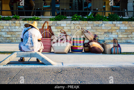 Mexikanischer Straßenhändler, der Taschen verkauft und vor einem teuren Restaurant wartet. Beispiel für wirtschaftliche Ungleichheit. Stockfoto