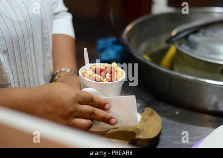 Esquites, mexikanische Street Food bestehend aus Mais in eine Schale mit verschiedenen Toppings, Erdnüsse in diesem Fall. Stockfoto