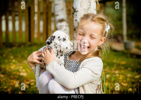 Kleiner Hund mit glücklicher Besitzer verbringen einen Tag im Park spielen und Spaß haben. Lustige Foto des lachenden Mädchen, sie umarmen und spielen mit schönen Dalmatiner Welpe. Positive Emotionen von Kindern Spaß Spiele mit Home pet-outdoor. Stockfoto