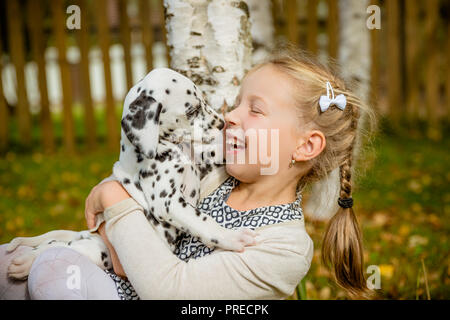 Kleiner Hund mit glücklicher Besitzer verbringen einen Tag im Park spielen und Spaß haben. Lustige Foto des lachenden Mädchen, sie umarmen und spielen mit schönen Dalmatiner Welpe. Positive Emotionen von Kindern Spaß Spiele mit Home pet-outdoor. Stockfoto