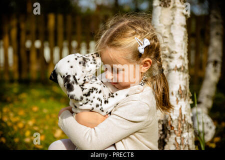 Kleine süße blonde Mädchen spielen mit Ihrem Dalmatiner Welpe outdoo, an sonnigen warmen Herbst Tag. Versorgung der Haustiere Konzept. Kind Küsse, umarmte ihre Hund, das Konzept des Kinder- und Hund Emotionen, der Freundschaft. Kopieren Sie Platz Stockfoto