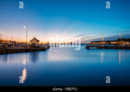 Helsinki, Finnland. Landschaft mit City Pier, Anlegestelle bei Sonnenaufgang. Blaue Himmel spiegelt sich in ruhigen Meer Wasser Oberfläche. Liegeplatz in der Beleuchtung am Abend oder Stockfoto