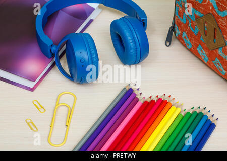 Die Schule liefert. Schule Rucksack, Buch, Buntstifte, Büroklammern und Kopfhörer auf Holztisch. Ansicht von oben. Zurück zum Konzept der Schule. Stockfoto