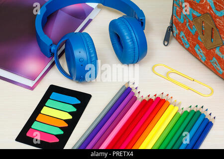 Die Schule liefert. Schule Rucksack, Buch, Buntstifte, Büroklammer, Farbe Lesezeichen und Kopfhörer auf Holztisch. Ansicht von oben. Zurück zum Konzept der Schule. Stockfoto