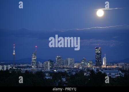 Vollmond und Wolken über der Skyline der Wiener SPÖ. Die moderne Stadt mit Wolkenkratzern mit beleuchteten Fenstern an düsteren Abend. Stockfoto