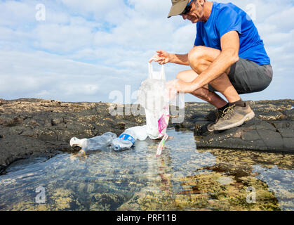 Ein Plogger/Jogger sammelt plastik Müll von Strand rockpool während seines morgendlichen Lauf Stockfoto